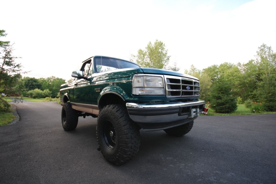 Front three-quarter photo of a green lifted Ford Bronco in a yard