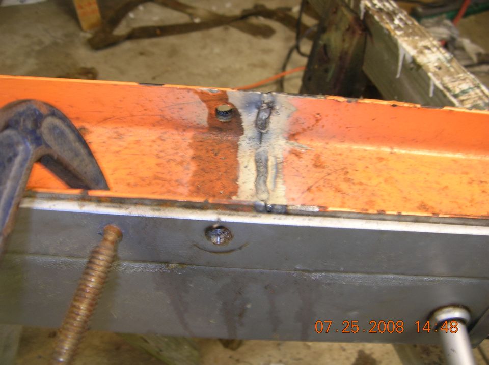Welded repair on orange metal beam with C-clamp and date stamp.
