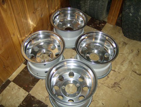 1990 Ford Bronco - Four polished aluminum alloy wheels with a five-lug bolt pattern are arranged in a cluster on a tiled floor. The wheels are leaning against…