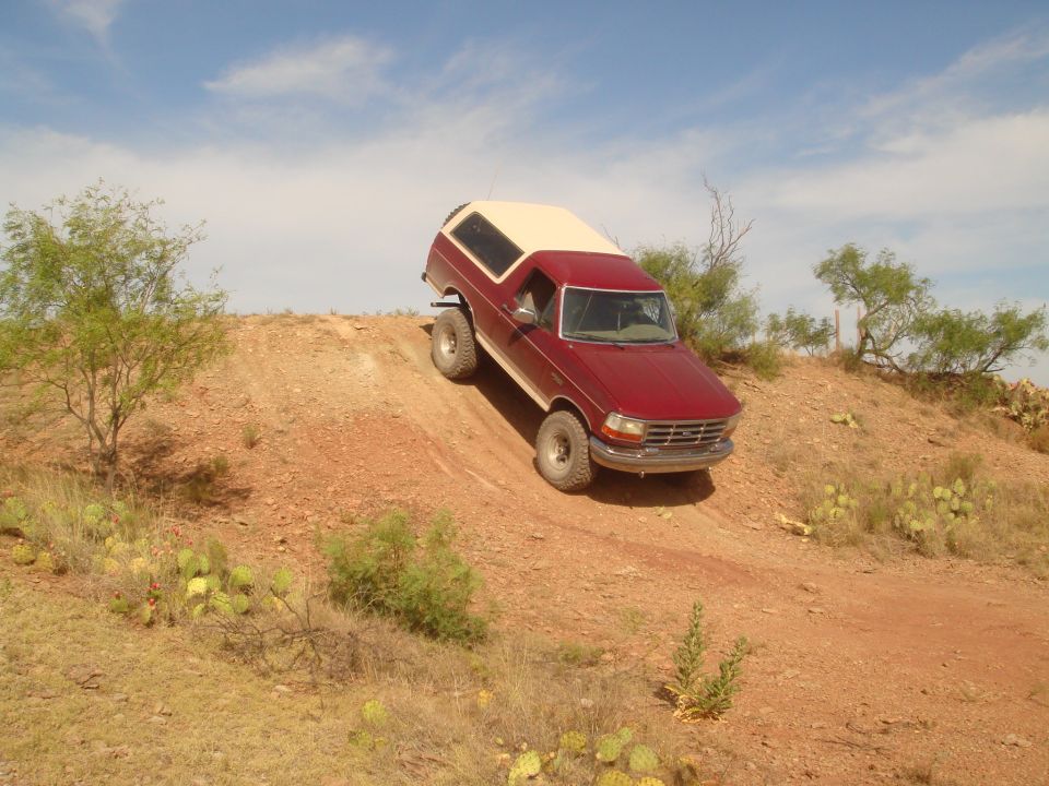 Red 1992 Ford Bronco driving up a dusty hill in a desert.