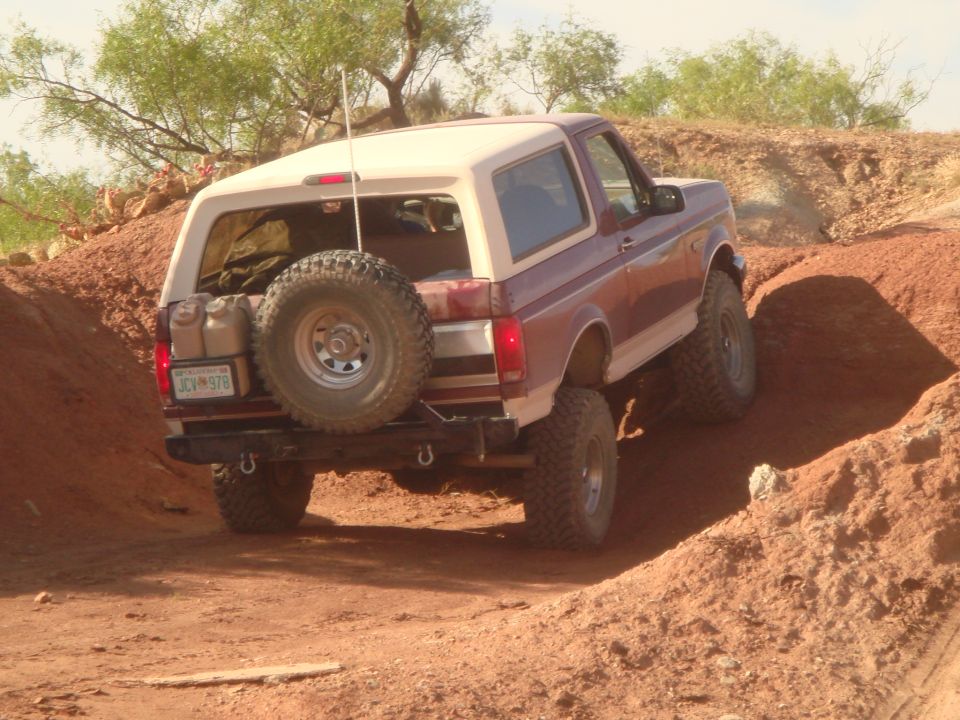 1992 Ford Bronco driving off-road on a dirt path, spare tire on back.