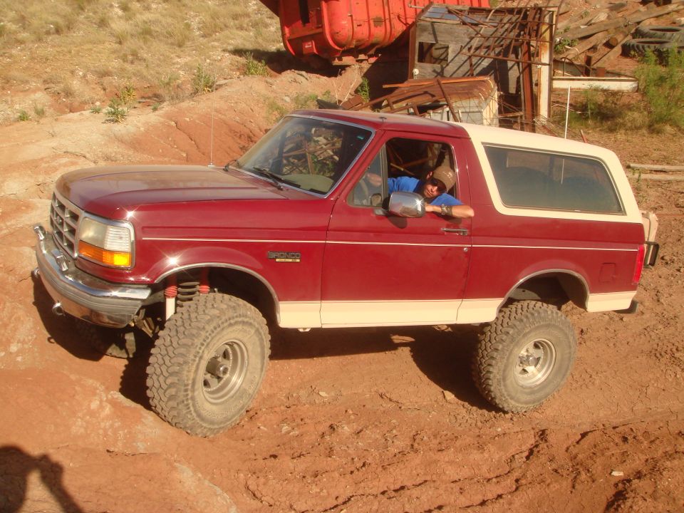 Red 1992 Ford Bronco with tan top and off-road tires on a dirt path.