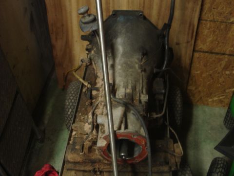 1989 Ford Bronco - The image shows the underside of a vehicle's transmission and drivetrain components, resting on a makeshift stand with wheels. The transmis…