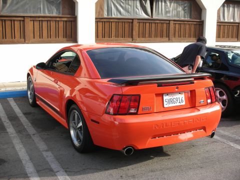 1998 Ford Crown Victoria - Rear view of an orange Ford Mustang Mach 1 coupe with a black spoiler and California plate in a parking lot.