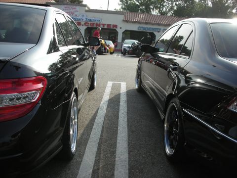 1998 Ford Crown Victoria - Photograph of two black Mercedes-Benz sedans parked facing a strip mall at a car meet.