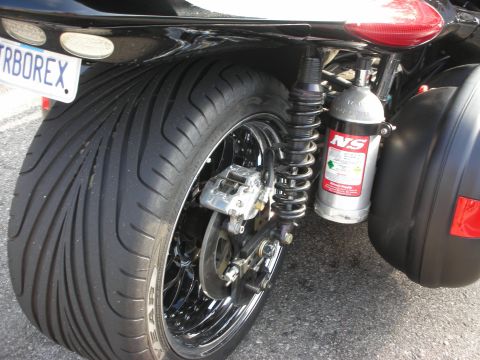 1998 Ford Crown Victoria - Close-up of a black three-wheeler's single rear wheel with coilover shock, brake caliper and a nitrous bottle.
