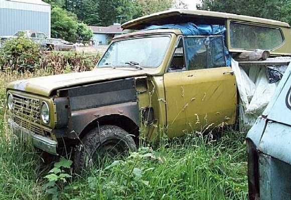 Yellow vintage International Scout SUV with body damage abandoned in tall grass