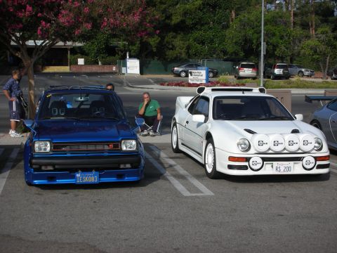 1998 Ford Crown Victoria - Photograph of a blue Toyota hatchback and a white Ford RS200 with rally lights at a show, not a technical document.