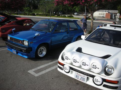 1998 Ford Crown Victoria - Photograph of the fronts of a blue hatchback and a white Ford RS200 rally car, not a technical document.