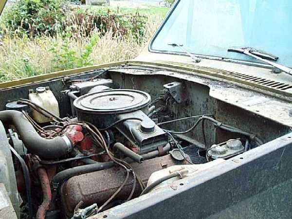 Engine bay of a Scout II with round air cleaner, red-painted V8, hoses and rust, hood open outdoors