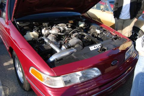 1992 Ford Crown Victoria - The engine bay of a red car features a heavily modified engine with twin turbochargers and custom intercooler piping.