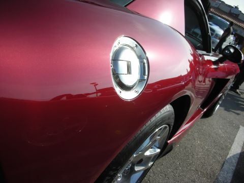 1998 Ford Crown Victoria - Detail of a chrome fuel filler door and rear quarter panel of a maroon sports car.