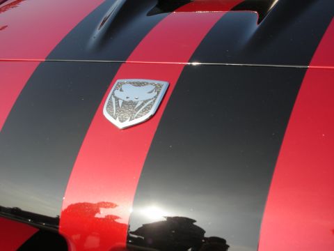 1998 Ford Crown Victoria - Close-up of the chrome Viper snake-head hood emblem on a red car with black racing stripes.