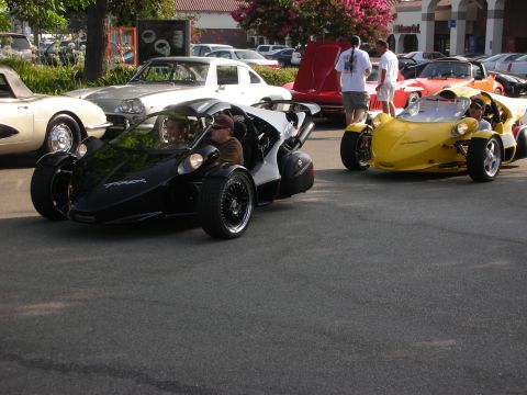 1998 Ford Crown Victoria - Black and yellow three-wheeled Campagna T-Rex roadsters driving in a car-show parking lot.