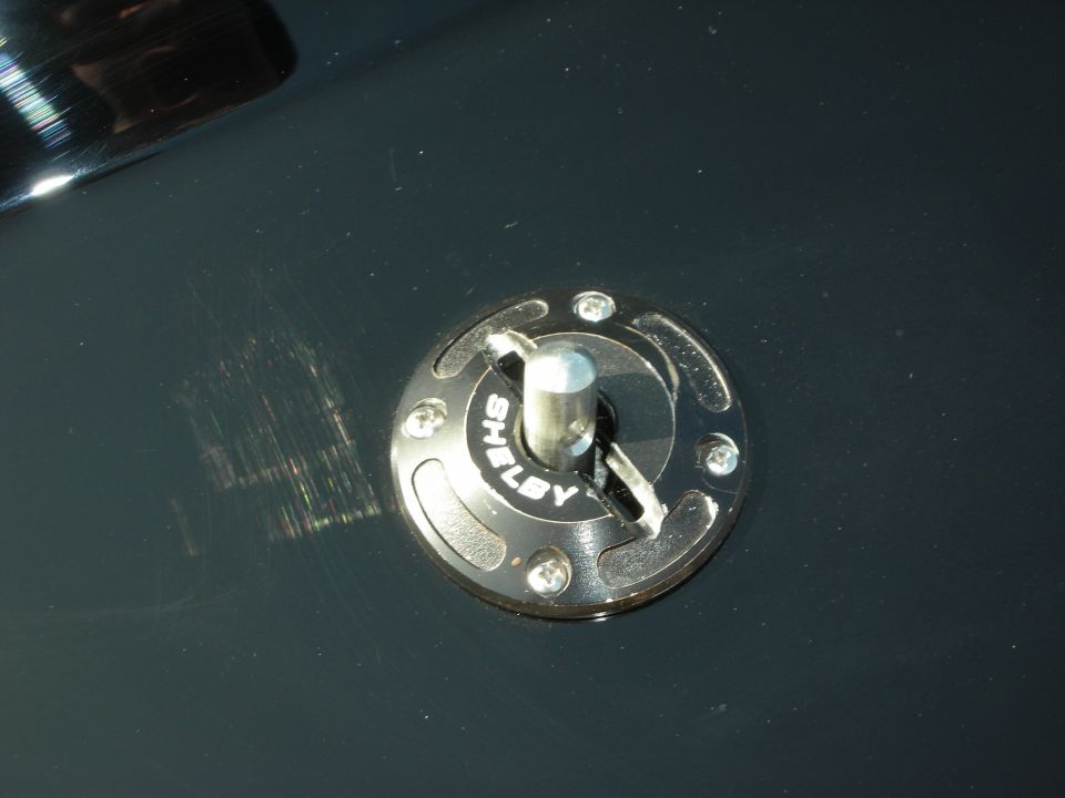 Chrome Shelby hood pin and latch on dark green painted body panel