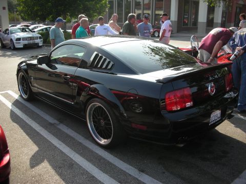 1998 Ford Crown Victoria - Photograph of a black Mustang from the rear at an outdoor car gathering, not a technical document.