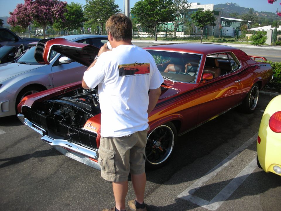 Man photographing a custom orange Mercury Cougar with hood open
