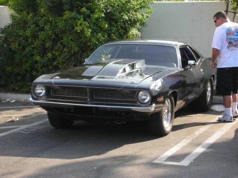 1998 Ford Crown Victoria - A black 1970 Plymouth Barracuda is parked outdoors, with a person standing nearby.