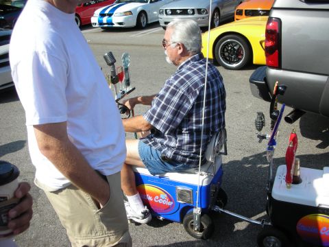 1998 Ford Crown Victoria - Photograph of a man on a novelty cooler scooter at a car show, not a technical document.