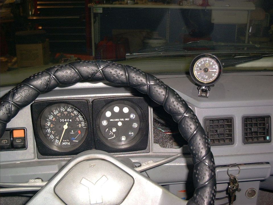 Yugo dashboard with wrapped steering wheel, 110 MPH speedometer, and aftermarket tach mounted on dash