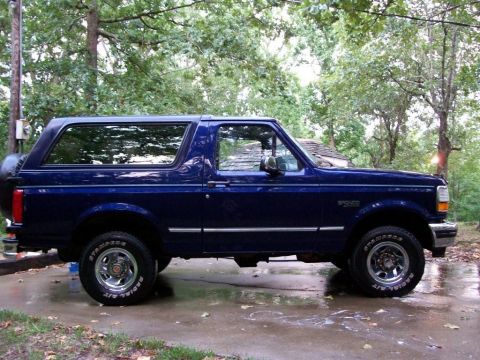 1994 Ford Bronco - Blue 1994 Ford Bronco parked on wet pavement with trees in the background.