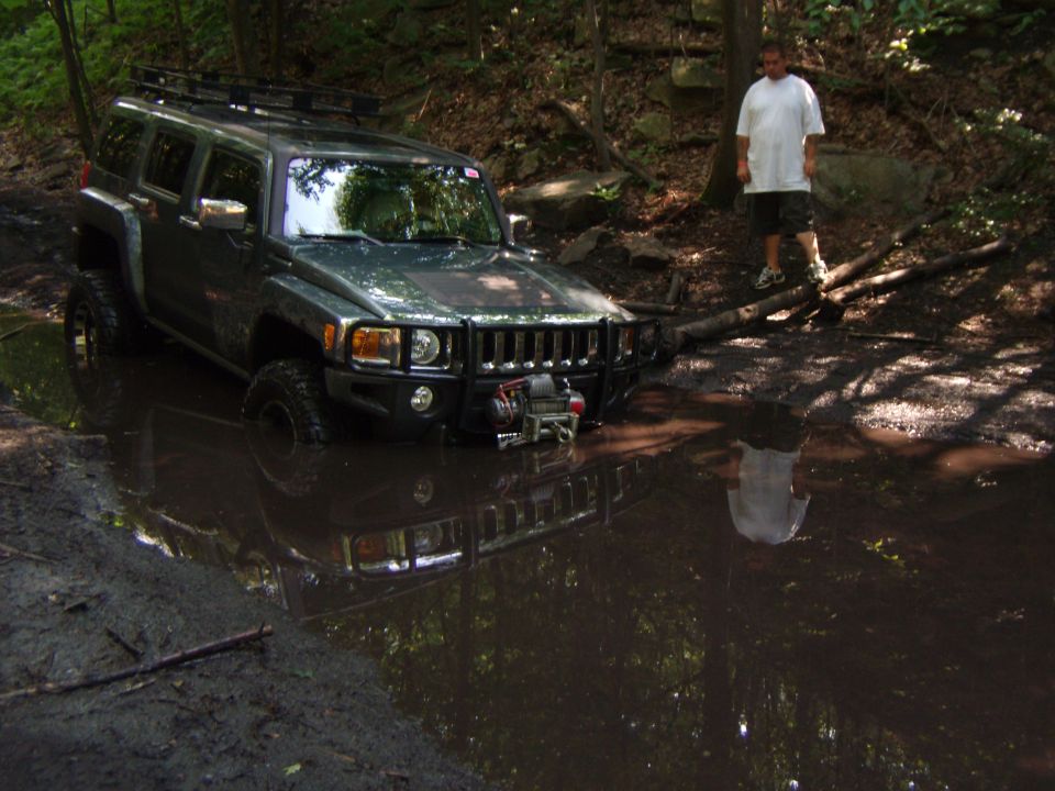 Hummer H3 stuck in a mud pit with a guy standing nearby