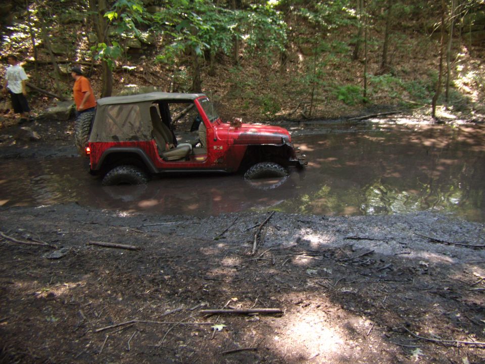Red 2003 Jeep Wrangler stuck in mud hole off-road