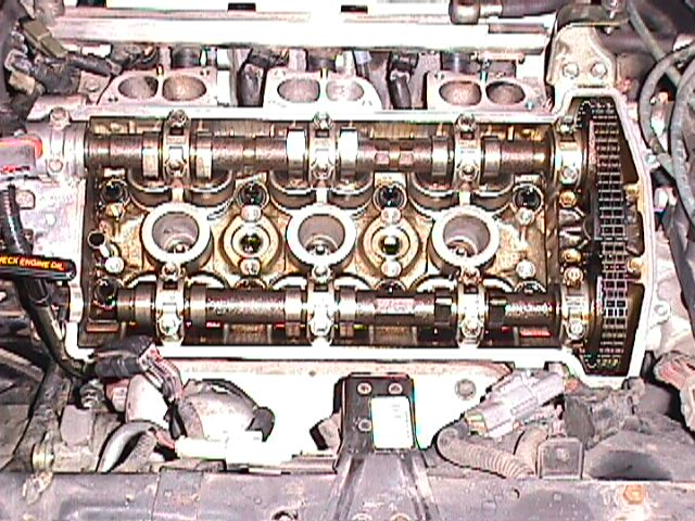 Engine with valve cover removed showing dual camshafts, valve train, and timing chain