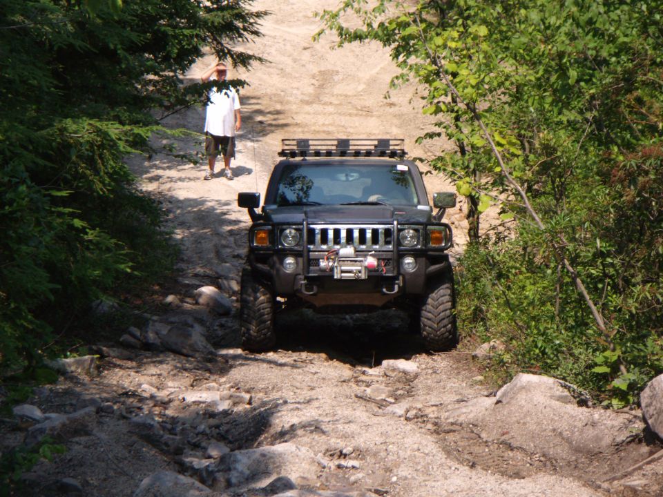 Black Hummer H3 with winch and roof rack on rocky trail. Visible "H3" badge