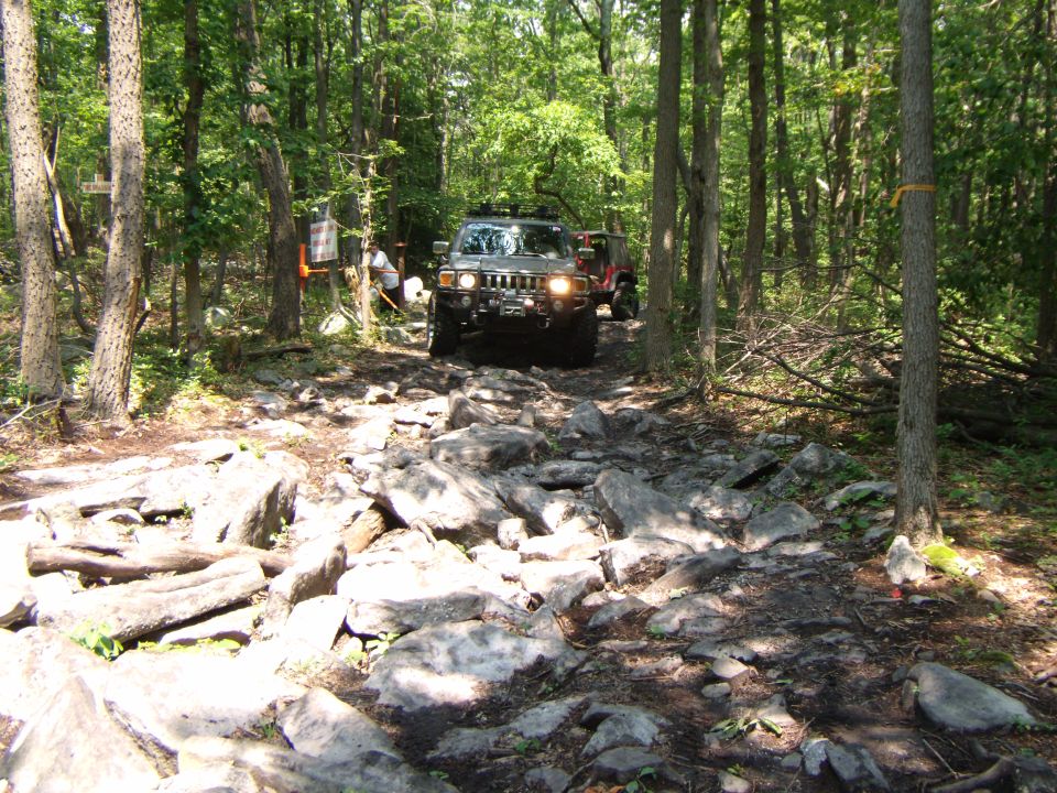 Hummer H2 driving over rocks in a forest. Another vehicle is behind it
