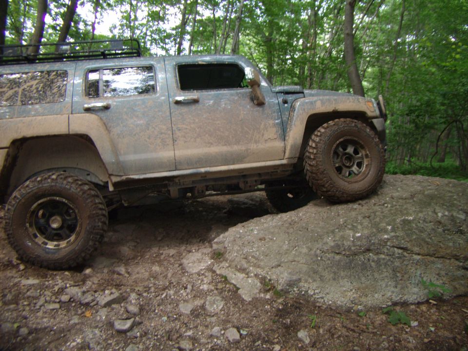Gray SUV climbing a large rock on a wooded trail