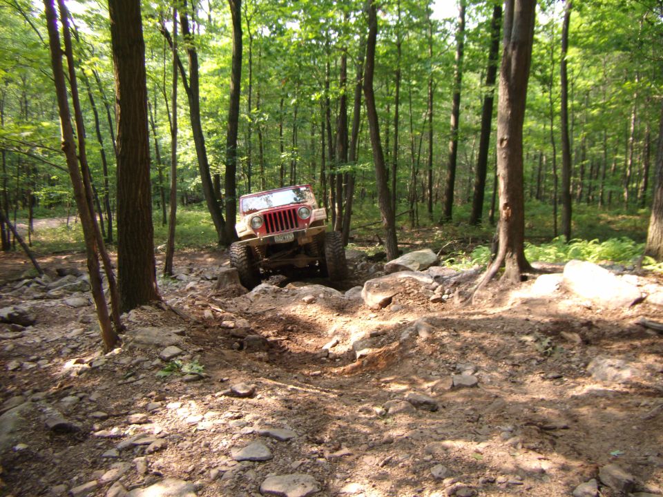 Red 2003 Jeep Wrangler navigating a rocky, wooded trail