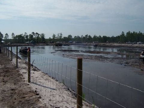 1989 Ford Bronco - Multiple vehicles are seen in a muddy water area with trees and a fence visible.