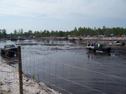 1989 Ford Bronco - Several trucks are navigating a muddy area, with spectators and trees visible in the distance.