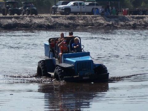 1989 Ford Bronco - A group enjoys a ride in a custom blue off-road vehicle through a muddy water area.