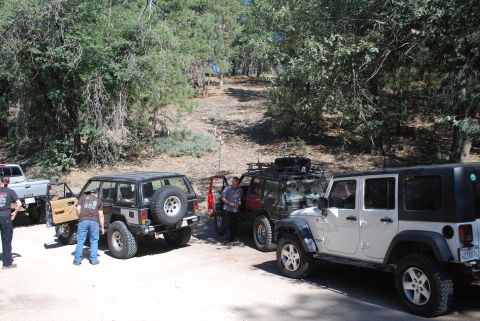 1996 Ford Bronco - Several SUVs are parked on a dirt road surrounded by trees, with people standing around them.