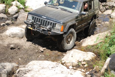 1996 Ford Bronco - Off-road Jeep Cherokee XJ tackling a challenging rocky and muddy path.