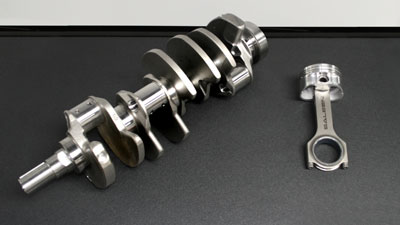 2007 Ford Mustang - A metal crankshaft and a piston with its connecting rod are displayed on a dark, textured surface.