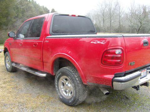 2007 Ford Mustang - Photograph of a red Ford F-150 crew-cab pickup with a bed cap parked on gravel.