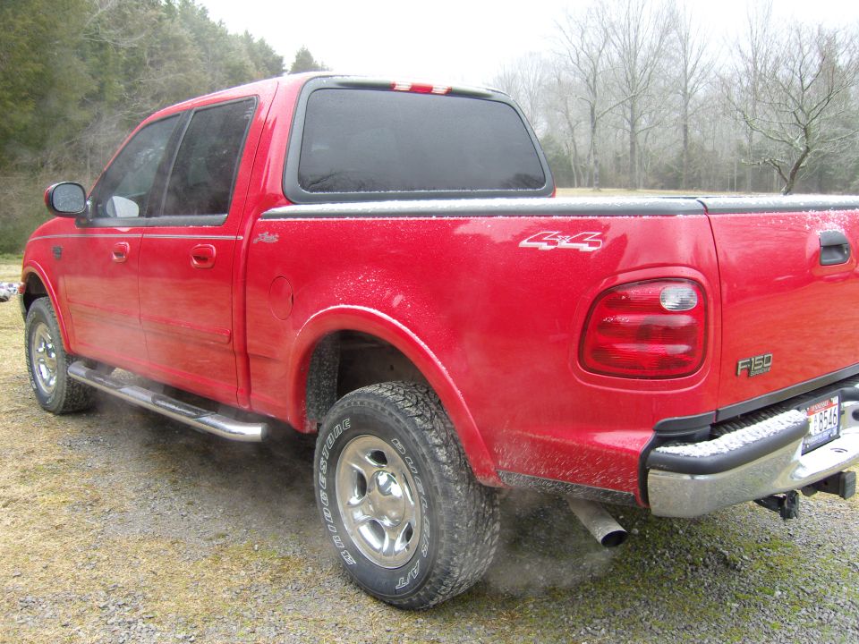 Red Ford F-150 SuperCrew 4x4 pickup with cap, rear three-quarter view