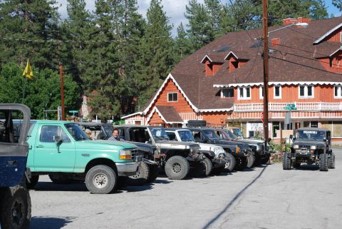1996 Ford Bronco - A line of modified Jeeps and a green Ford pickup truck are parked in front of a rustic building with a red roof. A man is visible in the dr…