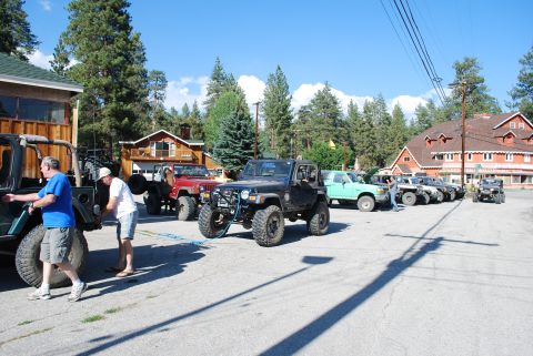 1996 Ford Bronco - Two men are preparing to tow a dark green Jeep Wrangler with a blue tow strap. Several other Jeeps and a green pickup truck are parked in t…