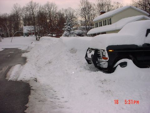 1979 Ford Bronco - A black truck is almost completely covered by snow after a heavy snowfall, with only the front grille and headlights partially visible.
