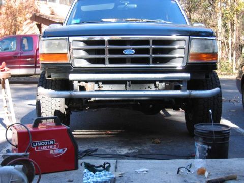 1993 Ford Bronco - Front view of a black Ford truck with a chrome grille and a custom bumper, parked outdoors with a red welder.
