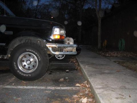 1993 Ford Bronco - The front of a black Ford Bronco is shown parked next to a sidewalk in the evening.
