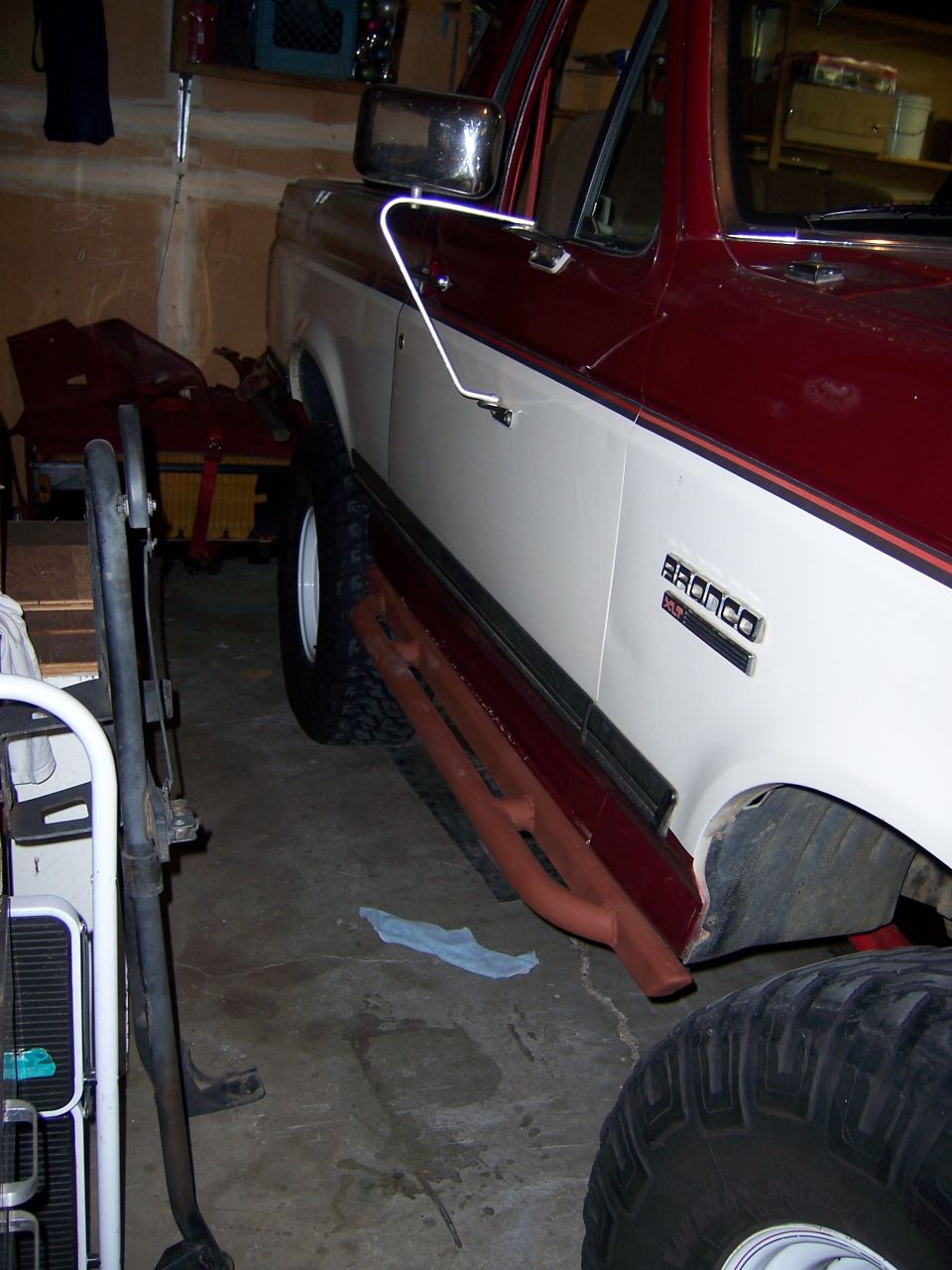 Side view of a red and white Ford Bronco with primered rocker panels
