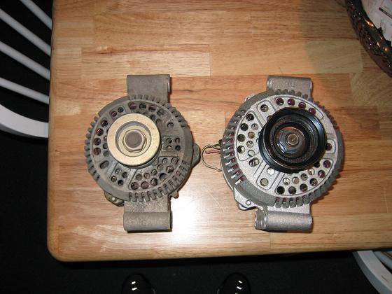 Two alternators on a wooden surface. One is older and grayer, the other is newer and shinier