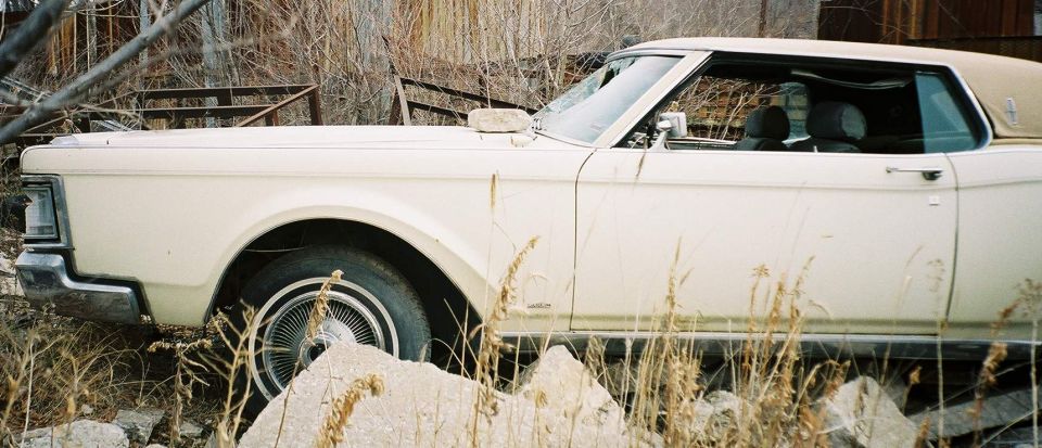 Cream 1969 Lincoln Mark III coupe with tan vinyl top parked in weeds and rocks, side view