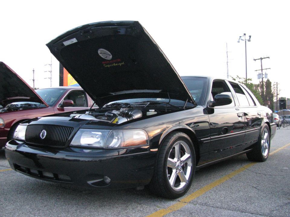 Black Mercury Marauder sedan with open hood showing supercharger at a car show