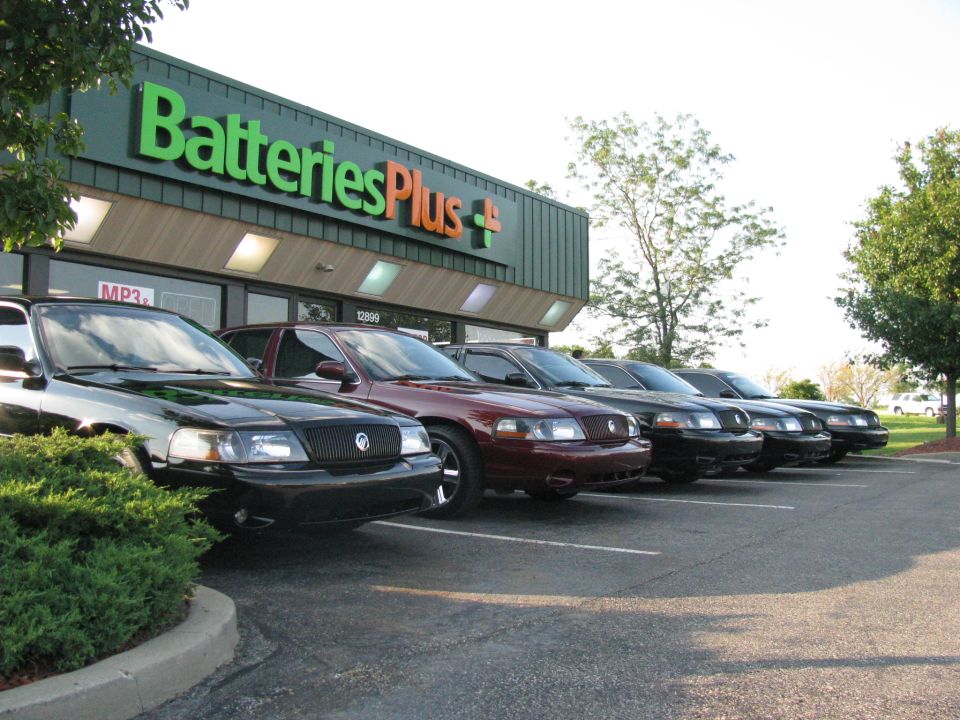 Several dark sedans parked in front of a Batteries Plus store.